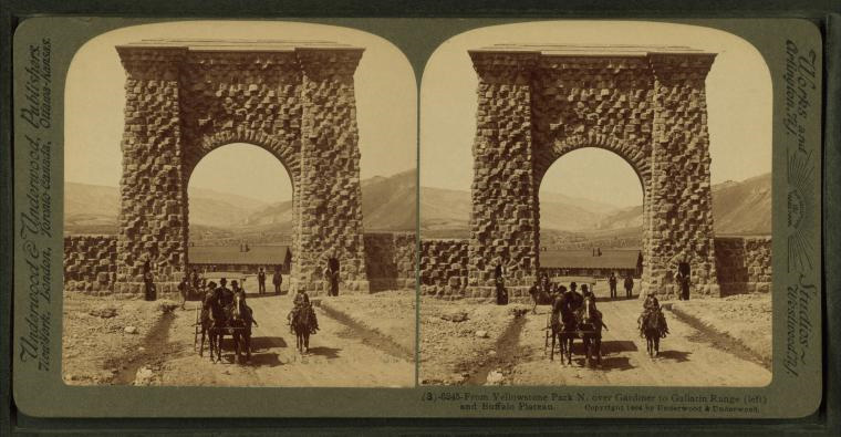 A historic image of a horse and buggy going through a stone arch at Yellowstone park.