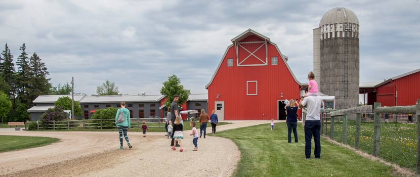 people walking on a dirt road toward a red barn.
