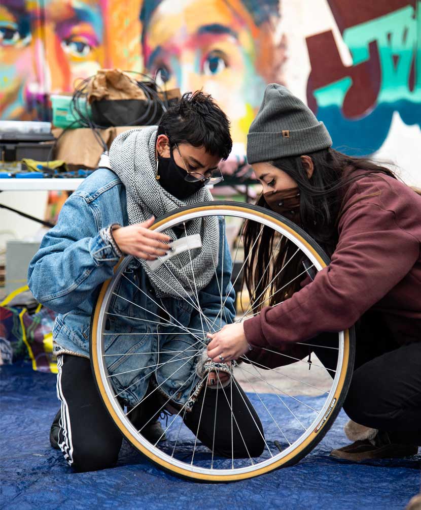 Two people in masks make repairs to a bike wheel.