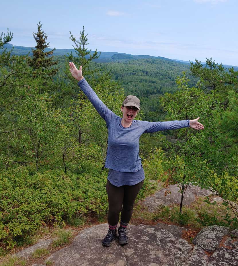 A woman spreads her arms wide and smiles as she stands on a mountain.