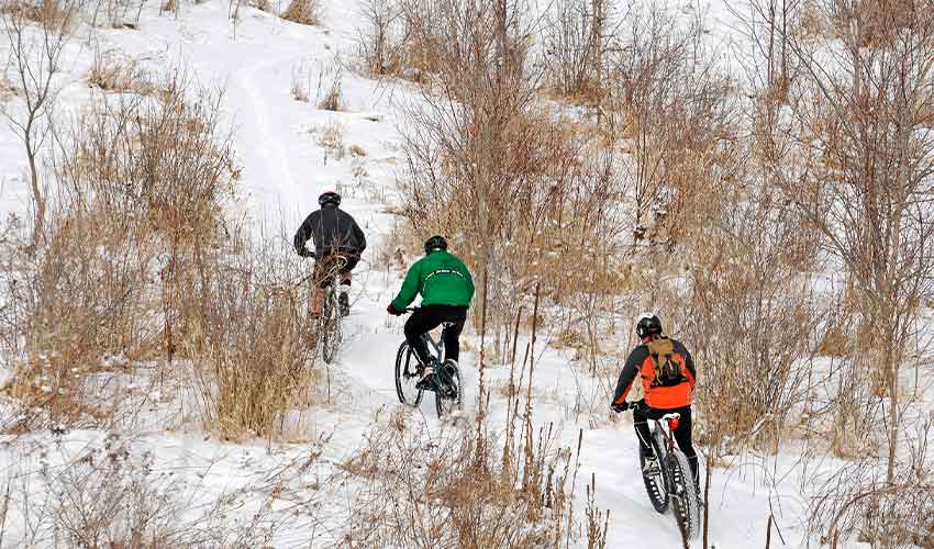 three bikers riding through snow on the singletrack at elm creek