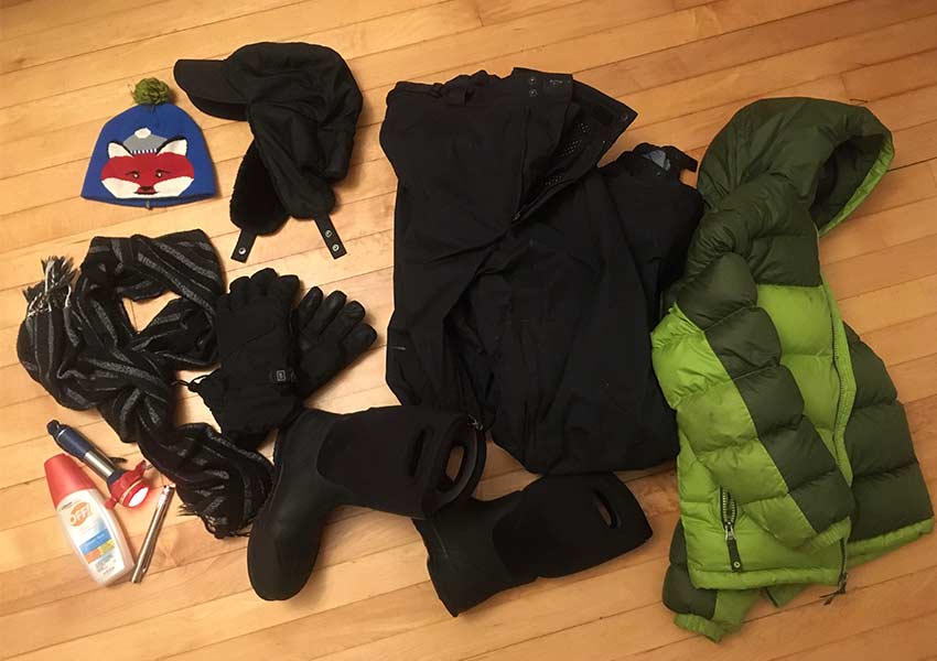 aerial photo of winter hat, coat, snow pants, gloves, bug spray and flashlight