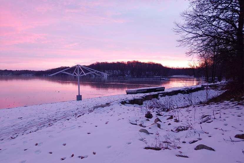 A pink and purple sunset over a lake in the winter.