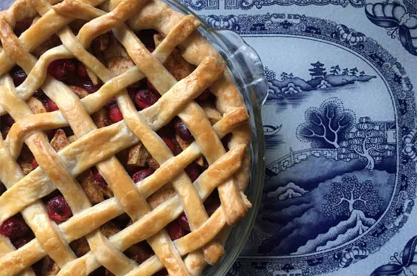 an apple cranberry pie with a lattice crust on a blue and white plate.
