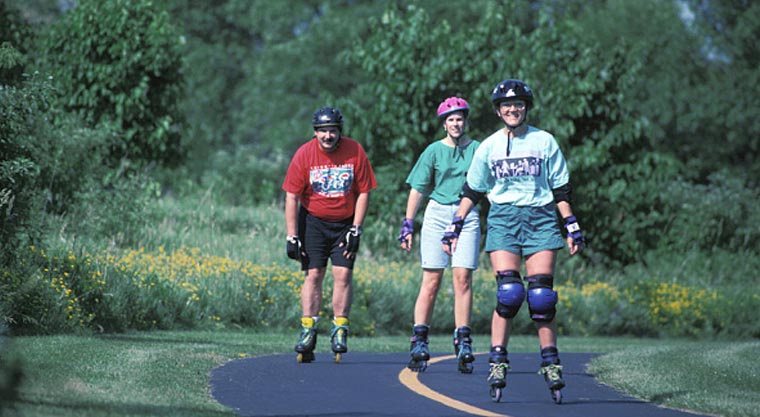 Three in-line skaters skate down a paved trail.