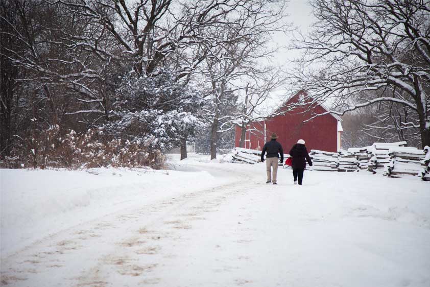 Two people walk toward a historic red barn in the winter at The Landing.