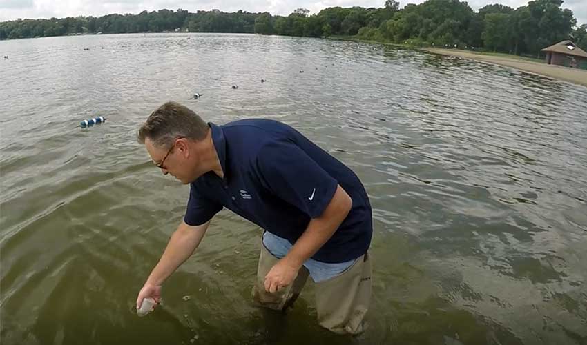 man standing in the lake with a vile to test for E. coli